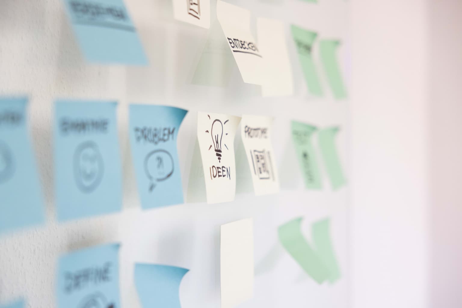 Bunte Post-Its mit verschiedenen Aufschriften kleben an einer Glastür.
